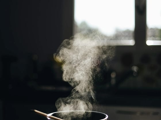 Pentolino da cucina con vapore su piano cottura, in una cucina illuminata dalla luce naturale.