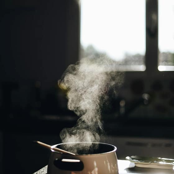 Pentolino da cucina con vapore su piano cottura, in una cucina illuminata dalla luce naturale.